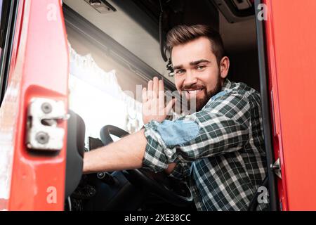 Smiling male truck driver sitting inside truck and waving with his hand Stock Photo