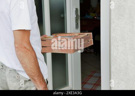 Two pizza boxes in hand of man standing on door. Pizza Delivery, Courier. Worker of food delivery se Stock Photo