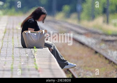 Lebensgefahr an der Bahnsteigkante Ein junges Mädchen hat sich auf eine Bahnsteigkante gesetzt, spielt mit ihrem Handy und befindet sich somit in großer Gefahr. *** Danger to life at the edge of the platform A young girl has sat down on the edge of a platform, is playing with her cell phone and is therefore in great danger Stock Photo