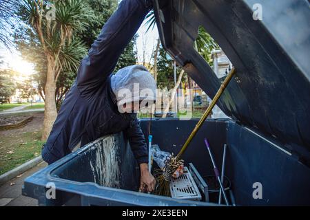 Homeless man looking into trash box in search for food on church background. Homelessness problem concept. Stock Photo