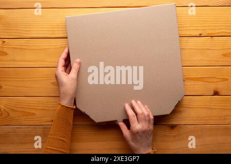 Pizza closed carton box in human caucasian hands on natural wooden table flat lay mockup with blank Stock Photo