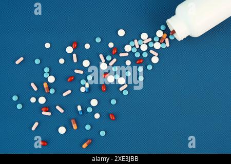 Group of assorted tablets and Capsules spilling out of white bottle. Blue Background. Line, way cour Stock Photo