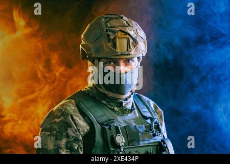 A portrait showcases a soldier in tactical gear against a backdrop of intense orange and blue smoke effects Stock Photo