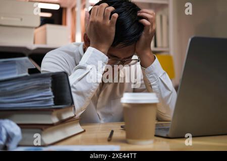 Asian young tired staff businessman using desktop computer having overwork project overnight in office. Stock Photo