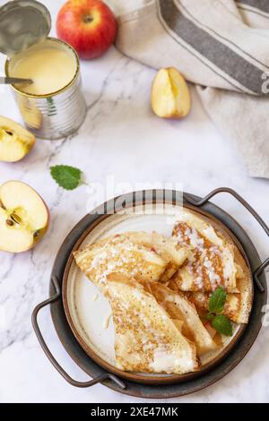 Celebrating Pancake day, healthy breakfast. Homemade sweet crepes with apples and condensed milk on a marble tabletop. Stock Photo