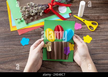 Child is holding easter congratulation card with basket easter eggs. Handmade. Project of childrens creativity, handicrafts, cra Stock Photo
