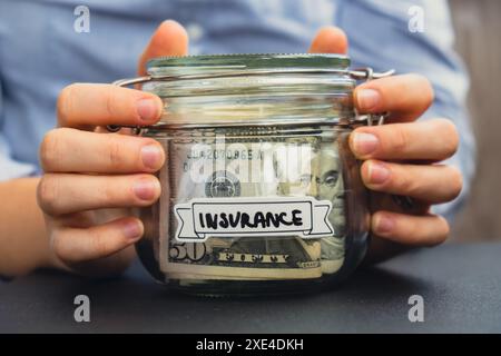 Unrecognizable woman holding Saving Money In Glass Jar filled with Dollars banknotes. INSURANCE transcription in front of jar. M Stock Photo