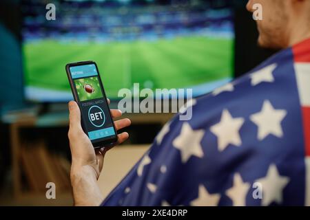 Over the shoulder shot of unrecognizable man watching football match betting on favorite team in app on smartphone Stock Photo