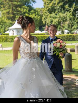 Beautiful bride and groom on a walk. The young bride stands half-turned and tenderly looks at the groom holding the wedding bouquet in his hands. Newl Stock Photo