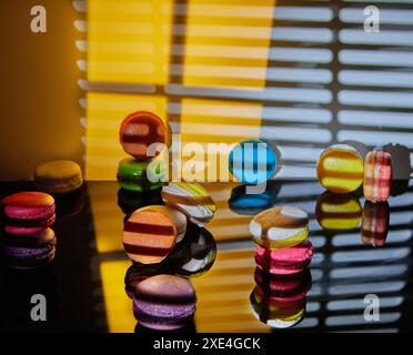 An assortment of bright macarons of different colors is displayed on a glass surface with a decorative abstract background illuminated in different pa Stock Photo