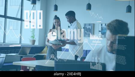 Image of graphs, map, cloud in laptop over diverse coworkers discussing reports in office Stock Photo