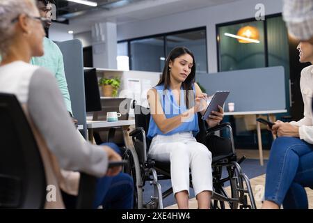 In office, woman in wheelchair taking notes on clipboard during team meeting Stock Photo