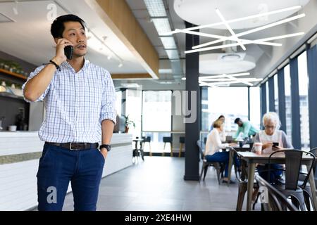 Talking on smartphone, man standing in modern office with colleagues working Stock Photo