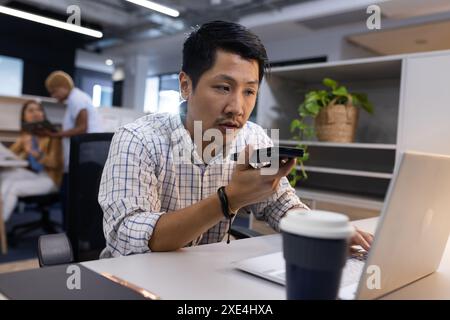 Using smartphone for voice command, man working on laptop in office Stock Photo
