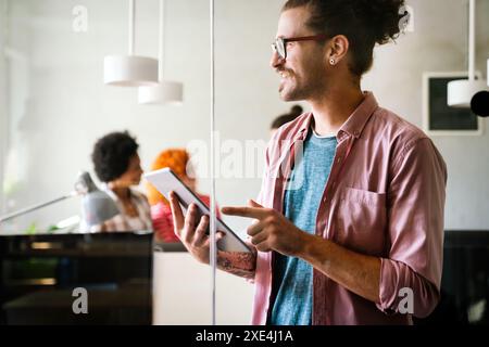 Happy young hipster businessman programmer holding a digital tablet and working in startup office Stock Photo