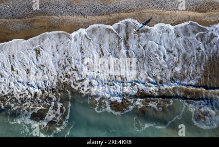 Aerial seascape of person walking in a beach. Stormy waves idyllic beach in winter. Stock Photo