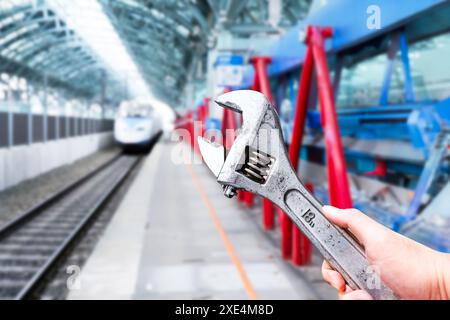 High speed train maintenance concept , Mechanic hand holding a adjustable wrench with high speed train station blurred on background Stock Photo