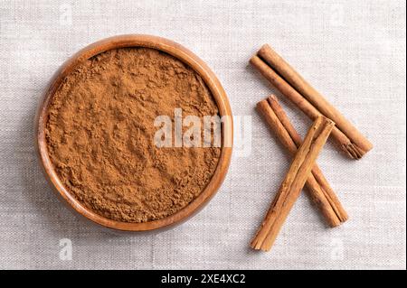 Ceylon cinnamon powder in a wooden bowl on linen. Ground bark of Ceylon cinnamon, Cinnamomum verum, and dried whole bark strips on the right. Stock Photo
