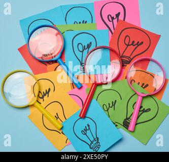 Drawn light bulbs on sheets of paper and a plastic magnifying glass, the concept of searching for new ideas. Stock Photo