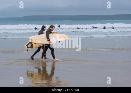 Two surfing friends carrying their surfboards walking along the shoreline on Towan beach in Newquay in Cornwall in the UK. Stock Photo