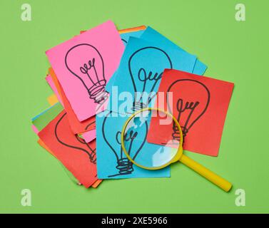 Drawn light bulbs on sheets of paper and a plastic magnifying glass, the concept of searching for new ideas. Stock Photo