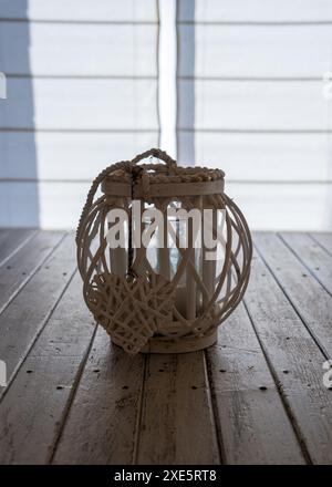 A wicker wooden candlestick with a heart stands on a wooden table against a white wooden wall. Table decoration, decoration Stock Photo