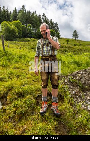 A farmer talking on his cell phone wears lederhosen made of chamois leather, a family heirloom that has survived several generations. . Hinterhölling, Großarl, Salzburg, Austria Stock Photo