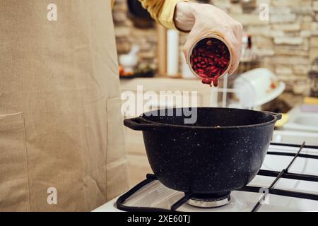 Unrecognizable man pours canned beans from tin can into a saucepan on a gas stove Stock Photo