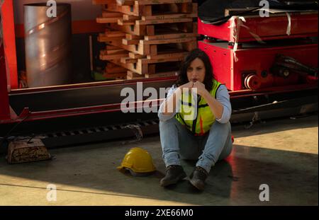 A young woman works in a warehouse storing rolls of metal sheet material. Sit down break and wipe off sweat a little before cont Stock Photo