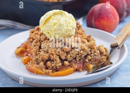 Peach Crisp or cobbler with brown sugar, cardamom and oat streusel on a white plate, served with scoop of vanilla ice cream, horizontal, closeup Stock Photo