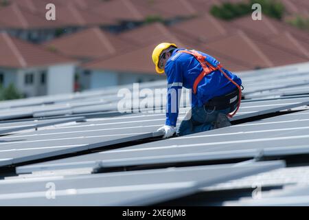 A technician is installing solar panels on the roof of the warehouse to change solar energy into electrical energy for use in fa Stock Photo