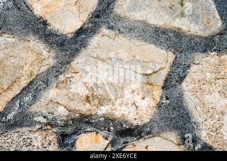 Close up of a stone wall with irregularly shaped stones and dark mortar lines. Stock Photo