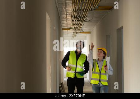 Male and female engineers working on construction site, they are monitoring the building's electrical system. Stock Photo
