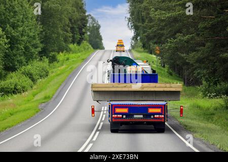 Heavy truck and trailer transporting wide load along highway with pilot vehicle ahead leading the way. Rear view, copy space. Stock Photo
