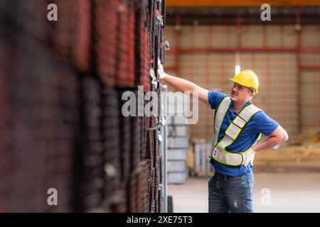 Portrait of a male worker wearing a safety vest and helmet standing on a steels pallet due to back pain from working in a factor Stock Photo
