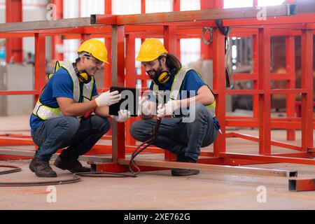 Portrait of two workers using digital tablet sit in front of the red steel structure Stock Photo