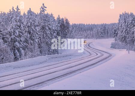 A car driving along a snow-covered road along the Finnish Lapland forest during a winter blue hour, Muonio, Finland, Europe Stock Photo