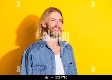 Photo portrait of pretty young guy cheerful toothy smile look camera wear trendy jeans outfit isolated on yellow color background Stock Photo