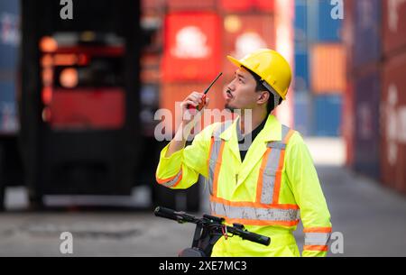 Portrait of a warehouse worker speaking on a walkie talkie with a coworker in an empty container warehouse while driving a scoot Stock Photo