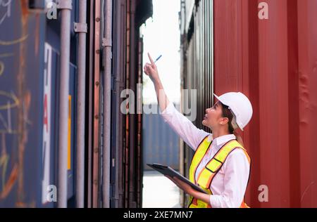 Workers in the import and export industries inspect the cargo of containers while holding a laptop and standing between them. Stock Photo