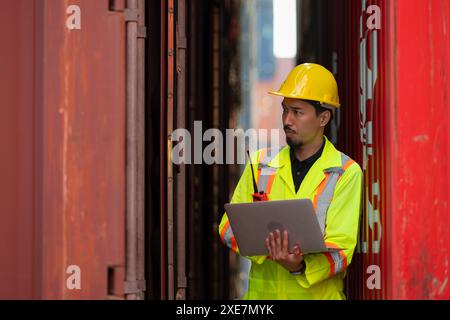 Workers in the import and export industries inspect the cargo of containers while holding a laptop and standing between them. Stock Photo