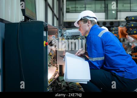 Technician working on the electrical control cabinet of robotic arm, Robotic arms industrial background Stock Photo