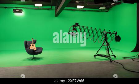 TV studio interior with green screen. Acoustic guitar on armchair being filmed with camera mounted on telescopic jib crane. Stock Photo