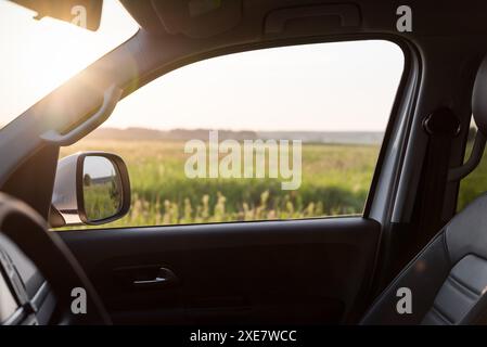 Car side window. Looking at the green meadow in the background through front passenger door. Stock Photo