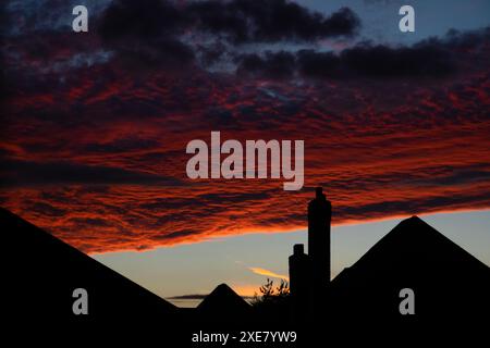 Sun shining onto evening cloud formations, setting on silhouetted suburb houses. Moody urban dusk silhouette. Stock Photo