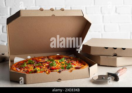 Large Pizza in open carton box and cutter on kitchen table closeup view Stock Photo