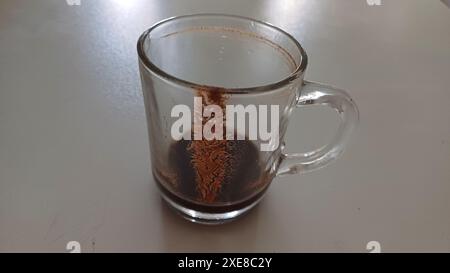 Mug of Turkish coffee with grounds and patterns left after drinking on white table. Dirty glass cup. Stock Photo