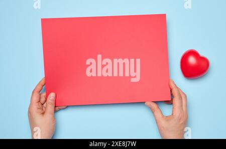 Female hands holding a blank red sheet of paper on a blue background Stock Photo