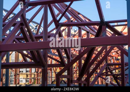 Geometric composition of red metal beams and a blue crane in a modern construction against a clear sky. You can see a chaos of construction with build Stock Photo