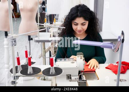 Dressmaker using professional overlock sewing machine in workshop studio. Equipment for edging, hemming or seaming clothes at ta Stock Photo